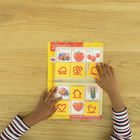 Text: "Die Farbe Rot". Zwei Hände blättern durch ein Kinderbuch mit roten Symbolen auf gelbem Hintergrund.