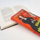 „Königin ohne Land“ von Jutta Jacobi liegt auf einem aufgeschlagenen Buch. Cover zeigt Kristina von Schweden.
