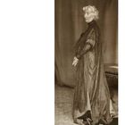 Text: "Cosima Wagner 1911". 
Eine elegante ältere Dame in einem aufwendigen langen Kleid, in einem formalen Setting.