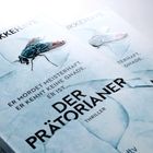 "Er mordet meisterhaft. Er kennt keine Gnade. Er ist... DER PRÄTORIANER. Thriller." zeigt Fliege auf hellem Hintergrund.
