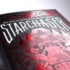 "Wen wird sie retten, wenn ihre Zeit abläuft? STARCHASER" steht oben. Darunter ein rotes Haus und ein Drache in Linien.