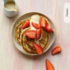 Frühstück: Ein Teller mit Pfannkuchen, garniert mit Erdbeeren und Soße. Daneben ein Krug mit mehr Soße.