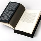Das geöffnete Buch zeigt zwei dicht beschriebene Seiten mit Text sowie einen schwarzen Buchumschlag mit weißer Schrift.