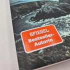Text: "SPIEGEL Bestseller-Autorin". Ein Küstenbild mit felsigen Klippen und schäumendem Meer im Hintergrund.