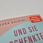 Text: "LAURA BALDINI" und "UND SIE". Ein rotes Sticker mit "SPIEGEL Bestseller-Autorin". Cover in Pastellfarben.