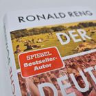 „RONALD RENG“, „SPIEGEL Bestseller-Autor“ in rotem Feld. Menschen sitzen auf einer Wiese, entspannte Atmosphäre.