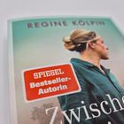 Text: "REGINÉ KÖLPIN", "SPIEGEL Bestseller-Autorin", "Zwischen". Frau im Profil, Haare hochgesteckt. Cover mit sanften Farben.