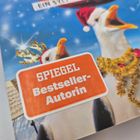 "SPIEGEL Bestseller-Autorin" auf orangener Fläche, lachende Gänse in Weihnachtsaccessoires vor blauem Himmel.