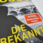 Text: "SPIEGEL Bestseller-Autor", "DIE UNBEKANNTE". 

Schattenriss einer Person vor einer Brücke.