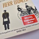 "SPITZENTEXTE: 'HERR DAIMLER', 'SPIEGEL Bestseller-Autor'. 
Illustration: Ein Mann mit Hut, beobachtet ein altes Auto."