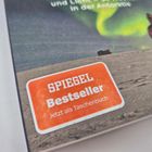 "SPIEGEL Bestseller Jetzt als Taschenbuch" in einem orangefarbenen Kasten; Hintergrund: Person in roter Kleidung und Polarlicht.