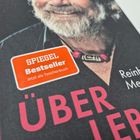Text: "SPIEGEL Bestseller Jetzt als Taschenbuch", "Reinhold Messner", "ÜBER LEBEN". Ein Porträt eines Mannes mit Bart.