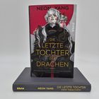 Buchtitel: "Die Letzte Tochter der Drachen" von Neon Yang, Illustration einer Person mit weißem Haar und einem roten Hintergrund.