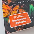 Text: "SPIEGEL Bestseller-Autorin." Ein orangefarbener Aufkleber über einem Schmetterlingsbild.