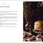 "Sunday Pancakes" oben in der Mitte. Links eine Zutatenliste. Rechts ein hoher Pfannkuchenstapel mit Ahornsirup.