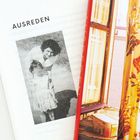 „AUSREDEN“ ist gedruckt. Links ein Schwarz-Weiß-Foto von zwei Personen; rechts ein Blick durch ein Fenster mit Vorhängen.