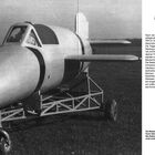 Erprobung. Ein futuristisch anmutendes Fluggerät auf einem Fahrgestell, im Hintergrund das Heck eines Flugzeugs mit der Nummer 4.