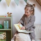 Regal mit Kinderbüchern, darunter „Stickpuzzle“. Kind sitzt lesend auf einem gemütlichen Sitzsack, bunte Wimpelkette hängt oben.