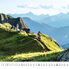 Ein Kalenderblatt für April zeigt einen Mountainbiker auf einem schmalen, grasbewachsenen Pfad inmitten von Bergen.