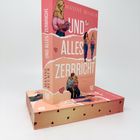 "Und alles zerbricht" von Maxine Reuker. Illustration einer Frau mit rosa Buch, zwei Personen sitzen zusammen.