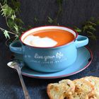 Text auf der Tasse: "Live your life. Live it, love it, enjoy it." Tomatensuppe in blauer Tasse mit Löffel und Brot.