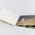 Ein geöffnetes Buch mit weißem Umschlag zeigt ein Gemälde von zwei Personen am Strand.
