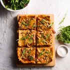 Sechs rechteckige Pizzastücke mit Rucola. Links oben: Schüssel Salat. Rechts: Rucola und Schale Salz. Unten: kleine Soßenschale.