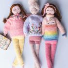Drei gestrickte Puppen mit geschlossenen Augen. Sie tragen bunte Strickpullover, einer mit Blumenmuster, einer mit Regenbogen.