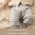 Text: "Ideal als Geschenk oder für die persönliche Erstausstattung." Baby trägt Strickkleidung mit beige-grauen Streifen.