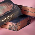 "MASKED BY NIGHTFALL" in goldener Schrift auf dunklem Hintergrund. Bücher mit dekorativen, floralen Mustern, rosa Seitenkanten.