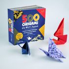 Auf einem Tisch steht eine Origami-Box mit drei gefalteten Papierfiguren in Blau, Rot und Lila.