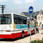 „TGA Auerbach“, „zuverlässiger Kundendienst“, Telefonnummer. Ein Bus mit Personen und Bushaltestellenschild daneben.