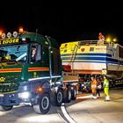 "EMIL EGGER" steht auf dem LKW. Nachttransport eines großen Schiffes, von Arbeitern begleitet.