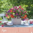 Text: "Apr" oben, Wochentage und Datumsangaben unten. Ein bunter Tulpenstrauß in einem Korb steht auf einem gedeckten Tisch.
