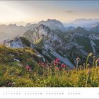 April-Kalenderblatt, Berglandschaft bei Sonnenuntergang, vordergründig bunte Blumen und Gras.