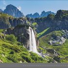 04 | APRIL. Eine Landschaft mit steilen Bergen, Wasserfall und weitläufigem, grünem Tal unter blauem Himmel.