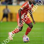 Dayot Upamecano in rotem Trikot auf dem Spielfeld. Großes "Vorabresabbildung" quer darüber, FC Bayern München Logo unten.