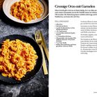 "Cremige Orzo mit Garnelen." Zwei Teller mit orangefarbenem Orzo-Gericht, goldenes Besteck, Rezept und Zubereitungstext.
