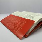 Weiße Schrift auf rotem Umschlagtext, darunter ein geöffnetes Buch mit sichtbarem Text auf den Seiten.