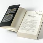 Linke Seite: Ein schwarzer Umschlag mit gelbem und weißem Text. Rechte Seite: Buchseite mit Kapitelüberschrift und Text.