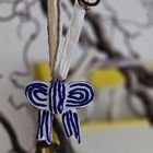 Ein blau-weißes, kunstvoll bemaltes Ornament hängt an einem Zweig. Dahinter sind verschwommene gelbe und braune Formen.