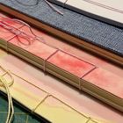 Mehrere übereinander liegende Notizbücher zeigen kunstvolle Bindungen mit bunten Schnüren in rosa und beige Tönen.