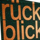 Text: "rückblick". Großer, orangefarbener Text auf dunkelgrünem, glitzerndem Hintergrund.