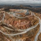 Es gibt keinen Text. Eine weite Landschaft mit einer riesigen Tagebaumine, terrassenartige Erdanlagen und umliegende Berge.