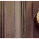 Auf einer hölzernen Tür ein runder, goldfarbener Türklopfer. Links daneben sind verblasste Sterne zu sehen.