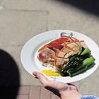 Ein Teller mit Reis, knusprigem Schweinefleisch, grünes Gemüse und gelbem Dip in einer Hand. Chinesische Zeichen darauf.