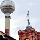 Links der Fernsehturm, rechts das Rote Rathaus mit Uhr und Berliner Flagge. Dächer im Vordergrund.