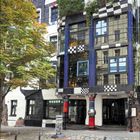 4 2024. Ein kunstvoll gestaltetes Gebäude mit unregelmäßigen Formen, bunten Fassaden und Bäumen, die aus Fenstern wachsen.