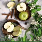 Grüne Äpfel und Blüten auf Zweigen, mit Zimtstangen und Anis, auf Holzplatten arrangiert. Kalenderleiste darunter.