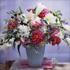 Ein blauer Vase mit einem großen Strauß aus weißen Lilien, rosafarbenen und roten Blüten auf einem Holztisch.